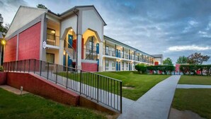 Um hotel de vários andares com fachada de tijolos, uma escadaria central e um gramado bem cuidado.