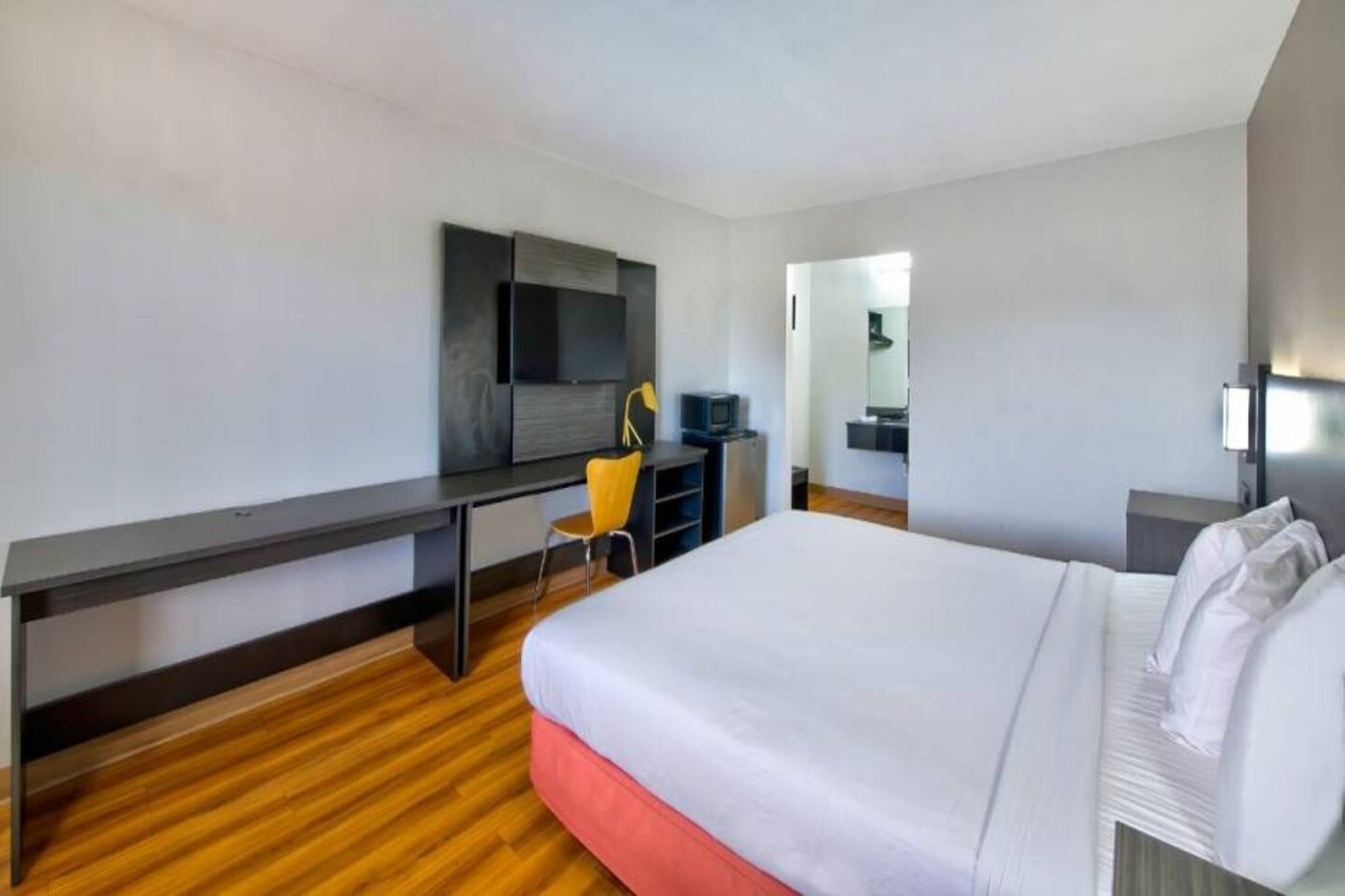 A hotel room with a bed, a desk, a chair, a television, and a mirror.