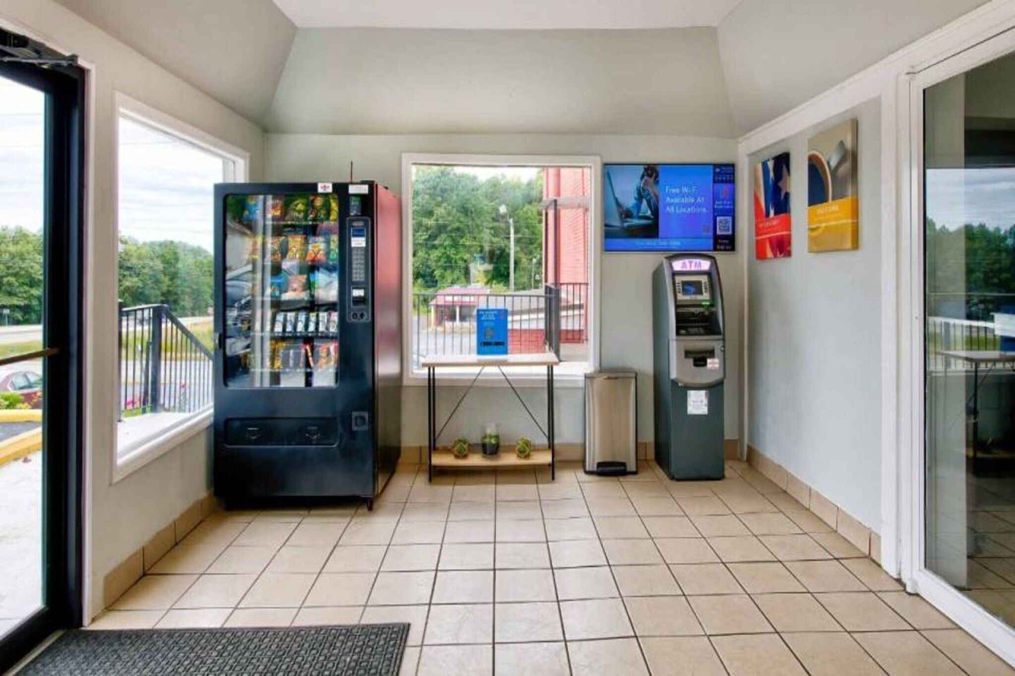 A clean, well-lit indoor area with a vending machine, an ATM, and a small table with a blue sign.