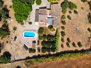 Vista aérea de una propiedad residencial con piscina, una casa grande y abundante vegetación.