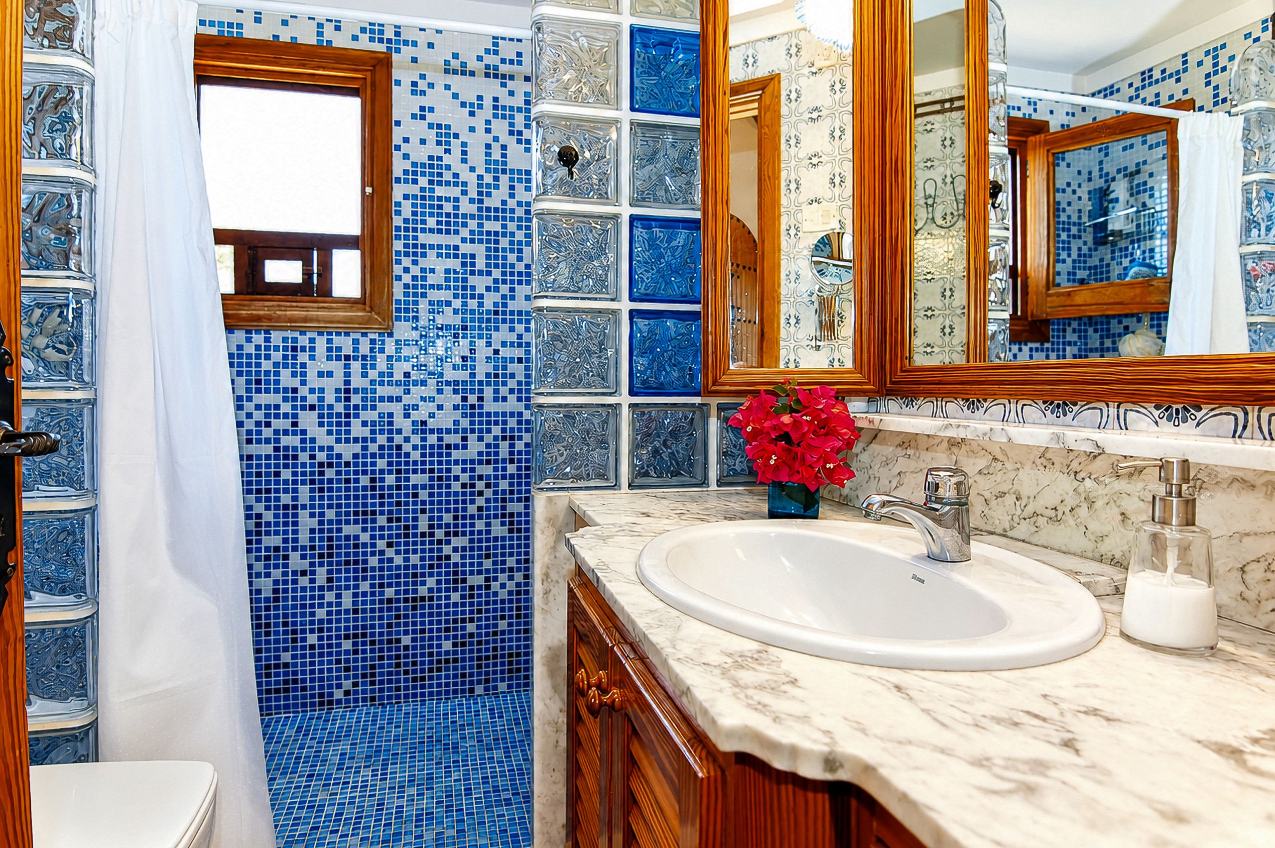 Un baño con pared de mosaico azul, un lavamanos blanco y un mueble de tocador de madera.