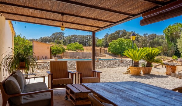 An outdoor patio with wooden furniture, a pool, and a view of the surrounding landscape.