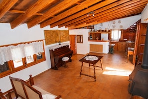 A rustic kitchen with wooden beams, a piano, and a dining table.