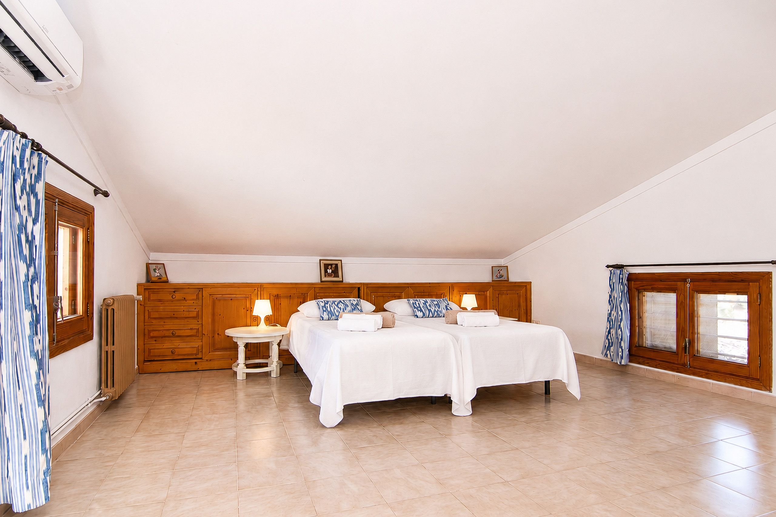 Una habitación con dos camas, un armario de madera, una mesita con lámpara y una ventana con cortinas.