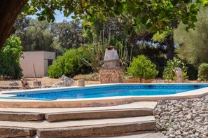 A swimming pool with a stone structure in the center, surrounded by various plants and trees.