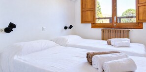 A hotel room with two single beds, a wooden window shutter, a wall-mounted light fixture, and a radiator.