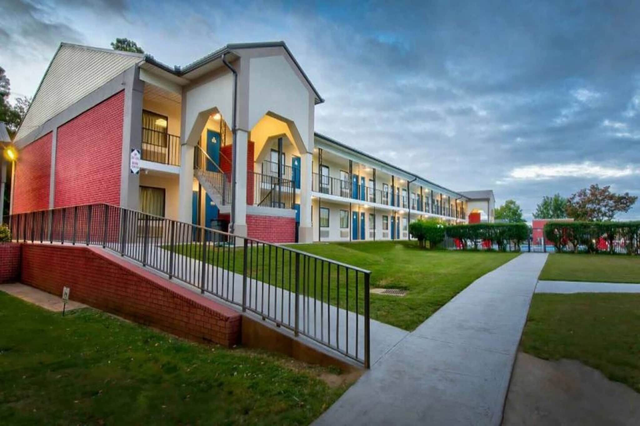 A multi-story hotel with a brick facade, a central staircase, and a well-maintained lawn.