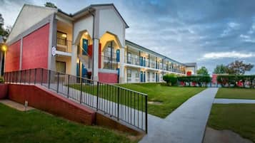 A multi-story hotel with a brick facade, a central staircase, and a well-maintained lawn.