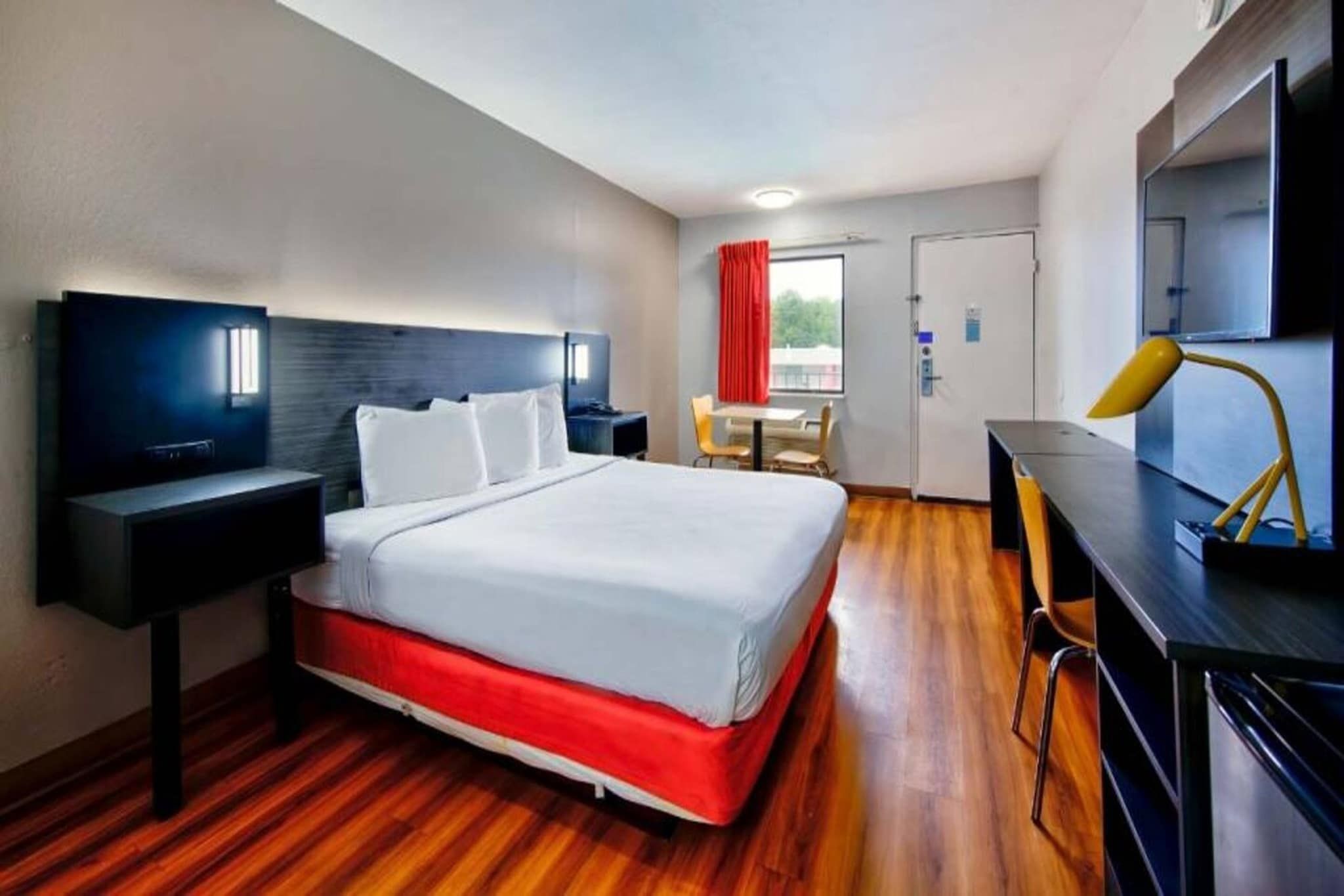 A hotel room with a bed, a desk, a chair, a TV, and a door.