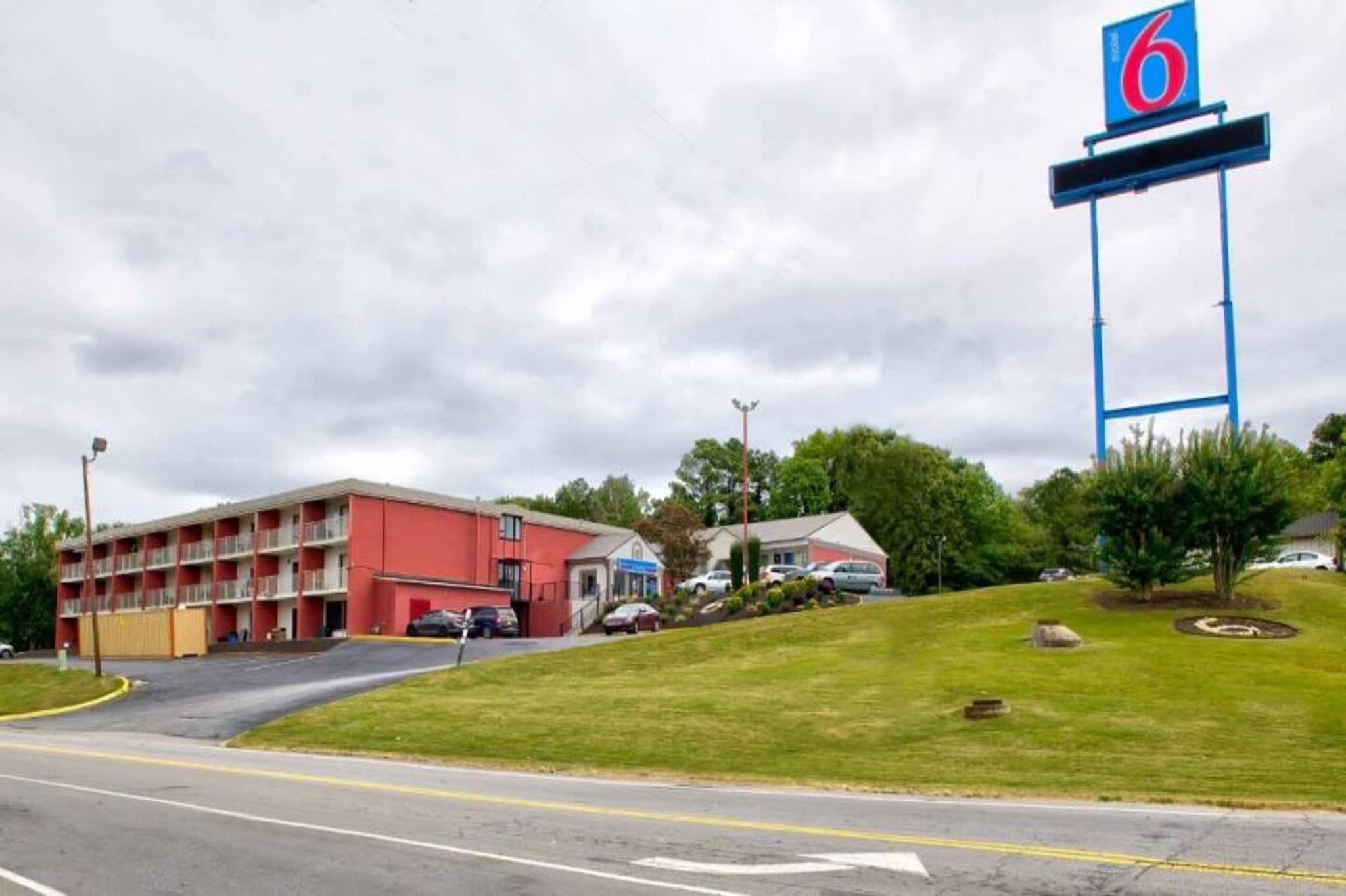 Ein Motel mit einem roten Gebäude, einem Parkplatz und einem großen blauen Schild mit der Nummer 6.