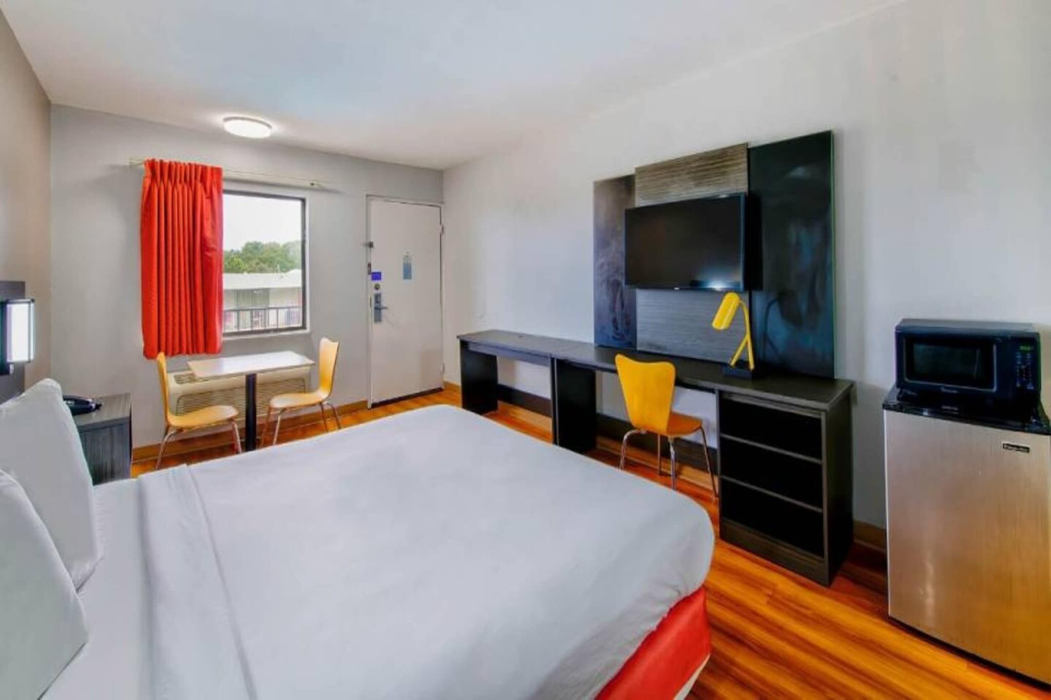 A hotel room with a bed, a desk, a television, and a refrigerator.