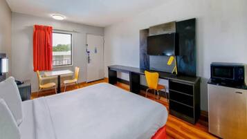 A hotel room with a bed, a desk, a television, and a refrigerator.