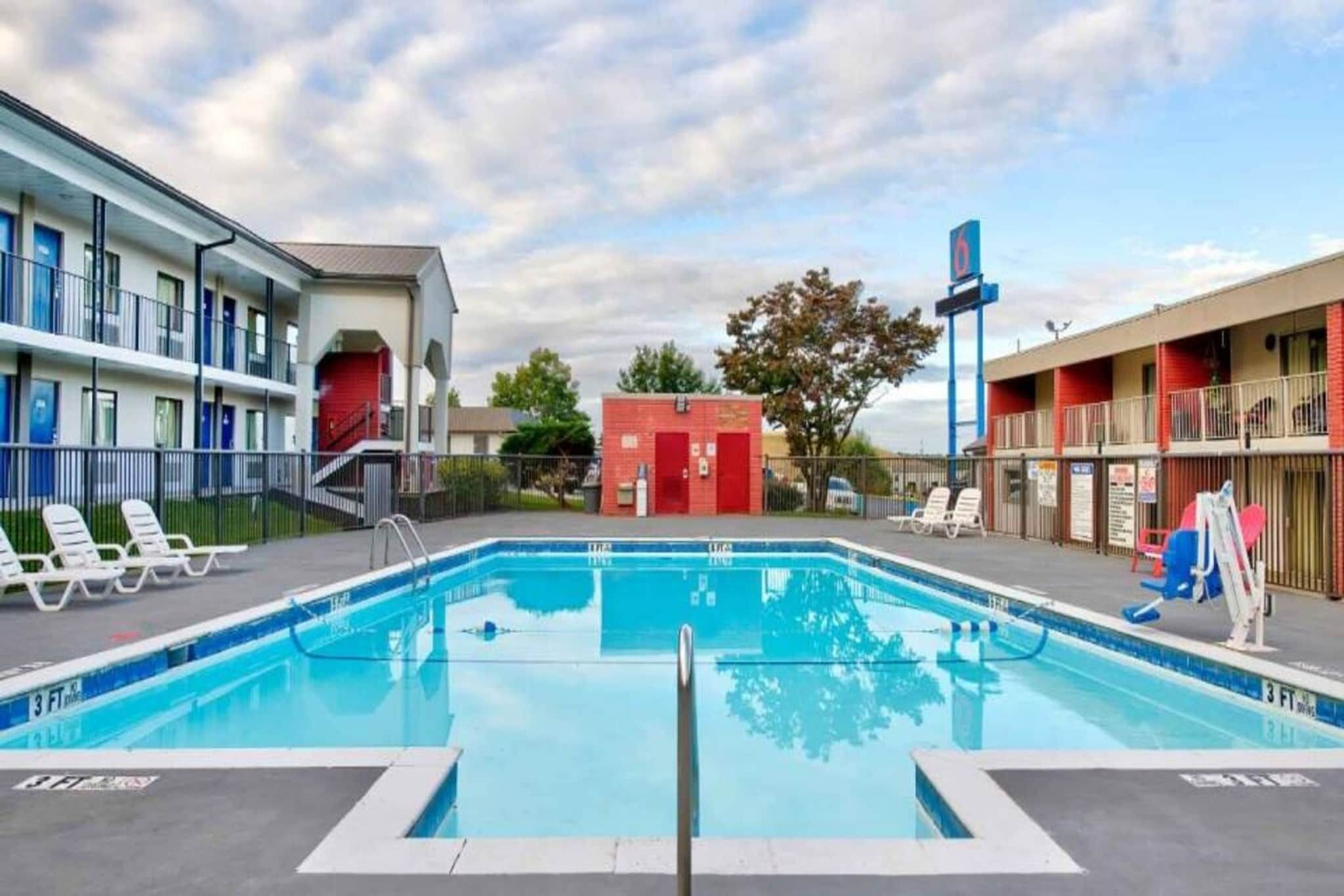 A swimming pool with a 3 FT depth marking, surrounded by lounge chairs, a red building, and a blue sign.