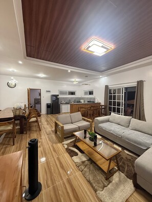 A modern living room with a wooden floor, a sofa set, a coffee table, and a dining area with chairs and a table.