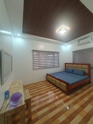 A bedroom with a bed, a desk, and a window with blinds.