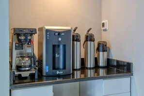 A kitchenette with a water dispenser, a coffee machine, and two stainless steel thermos cups.