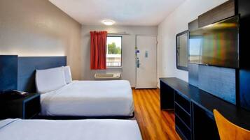 A hotel room with two beds, a TV, a desk, and a window with curtains.
