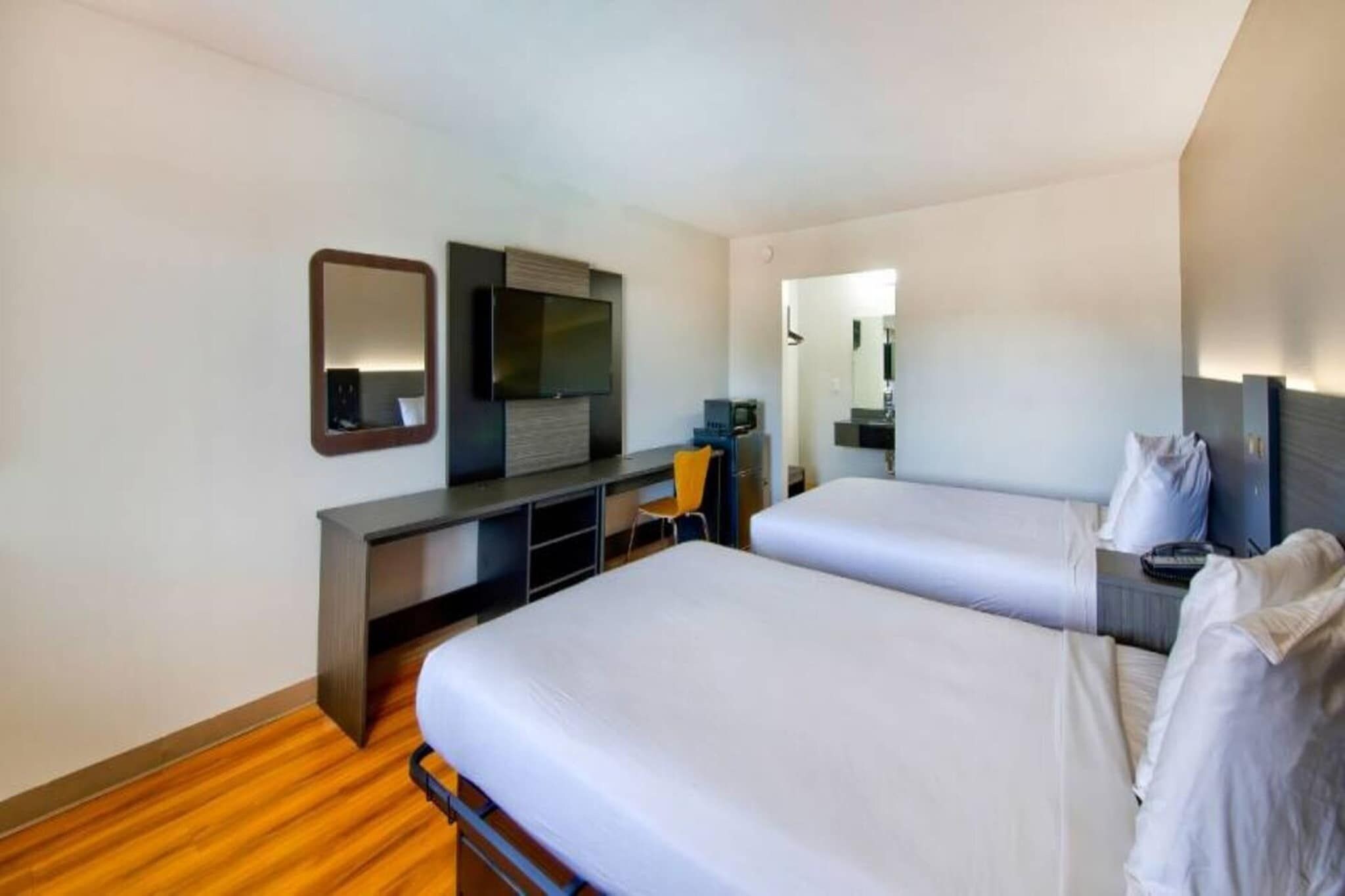 Una camera d'albergo con due letti, una scrivania, una TV e uno specchio.