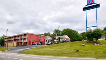 A motel with a red building, a parking lot, and a large blue sign with the number 6.