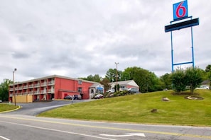 A motel with a red building, a parking lot, and a large blue sign with the number 6.