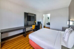 A hotel room with a bed, a desk, a chair, a television, and a mirror.
