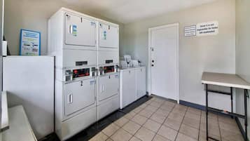 A laundry facility with multiple washing machines, a drying area, and a sign indicating the facility is not responsible for unattended items.