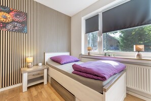 Un dormitori modern amb un llit, una taula de nit, una làmpada i una finestra amb vista a l'exterior.