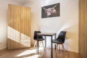 Une pièce comprenant une armoire en bois, une table avec deux chaises et un tableau encadré représentant un yak accroché au mur.