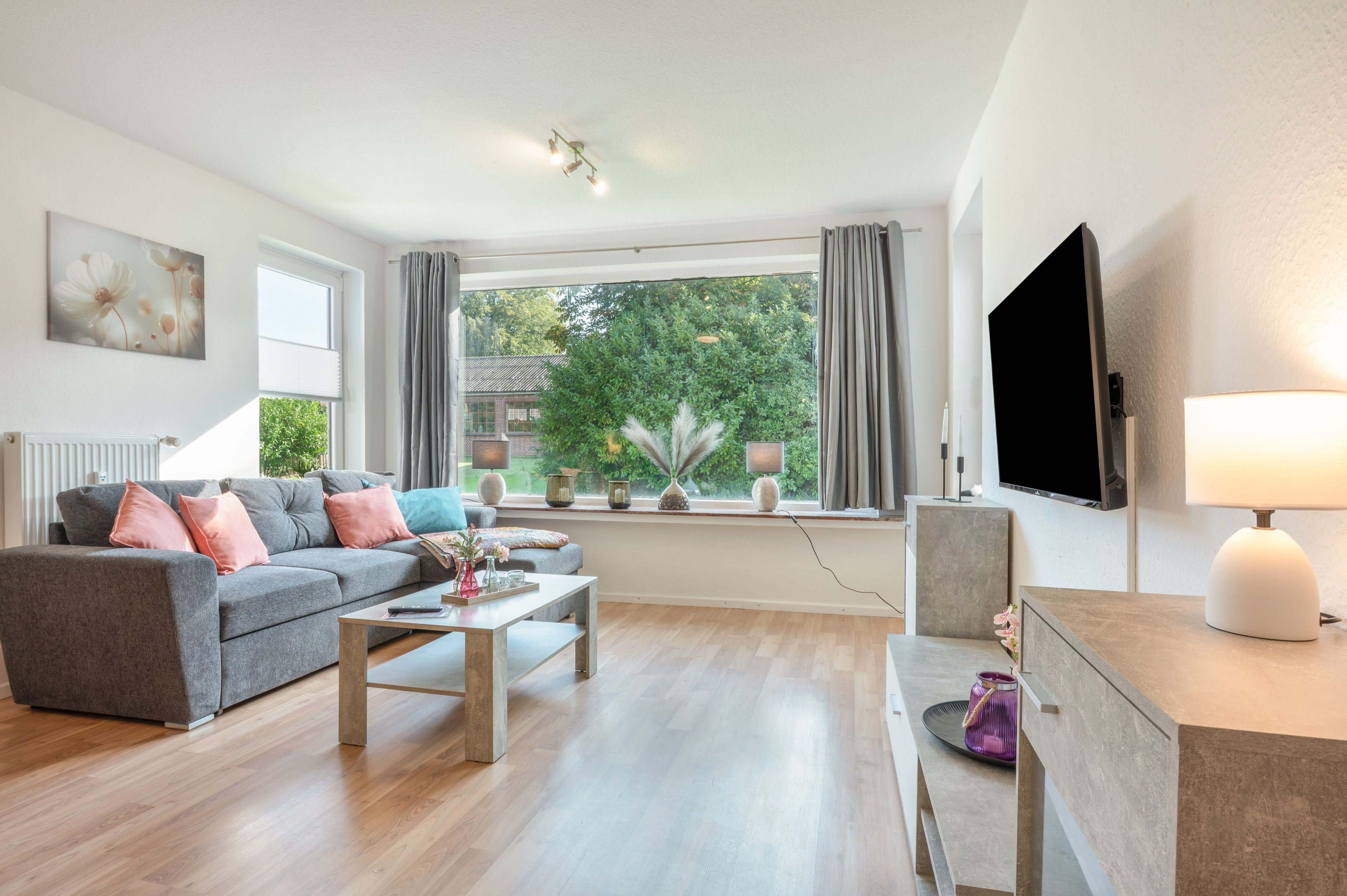 Ein modernes Wohnzimmer mit einem grauen Sofa, einem Couchtisch, einem Fernseher und einem Fenster mit Vorhängen.