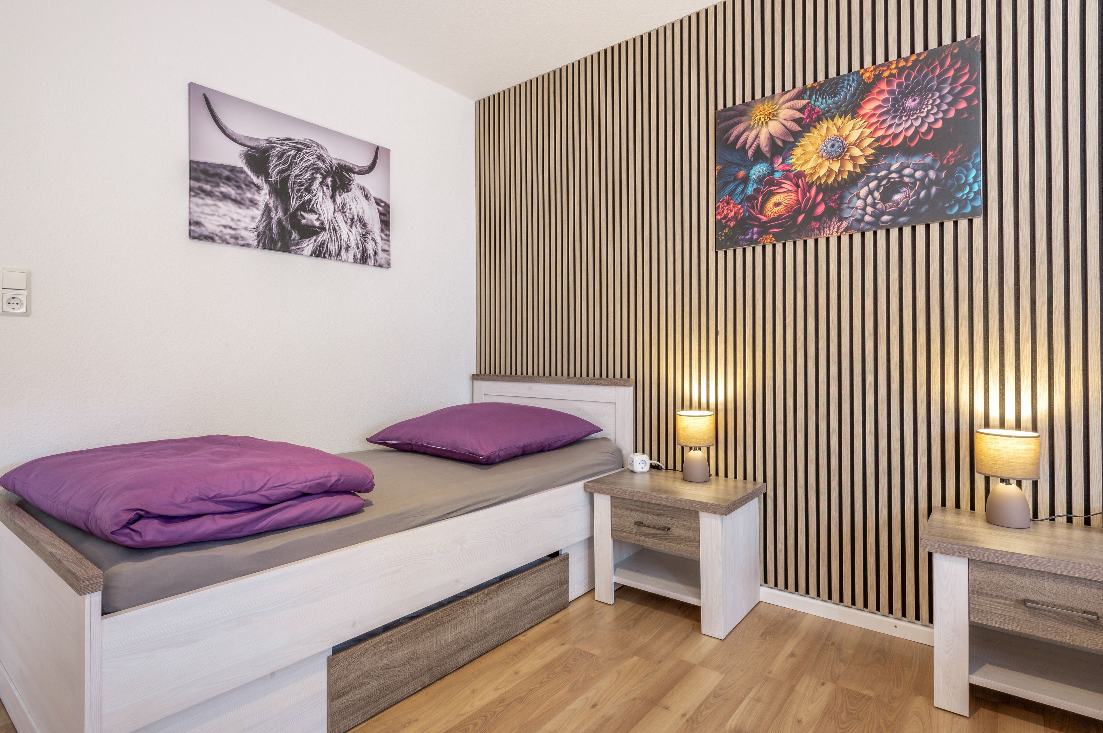 A modern bedroom with a bed, bedside tables, a lamp, and a wall with vertical wooden slats.