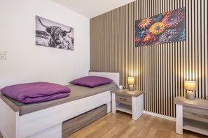 Un dormitori modern amb un llit, taules de nit, una làmpada i una paret amb llistons de fusta verticals.