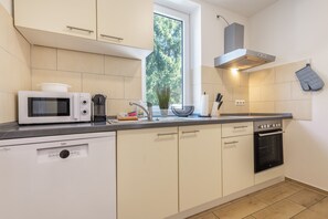 A modern kitchen with white cabinets, a built-in microwave, a stove, and a window providing a view of greenery outside.