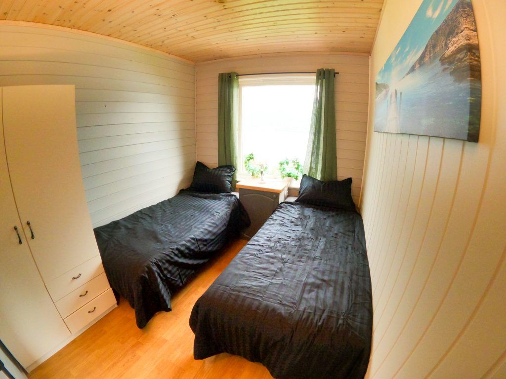 A room with two beds, a wardrobe, a window with curtains, and a painting on the wall.