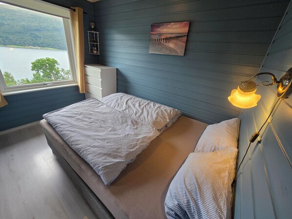 Une chambre à coucher avec un lit, une table de chevet, une étagère fixée au mur avec un verre à vin, et un tableau.