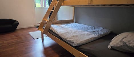 A bunk bed with a wooden ladder, a window with curtains, and a painting on the wall.