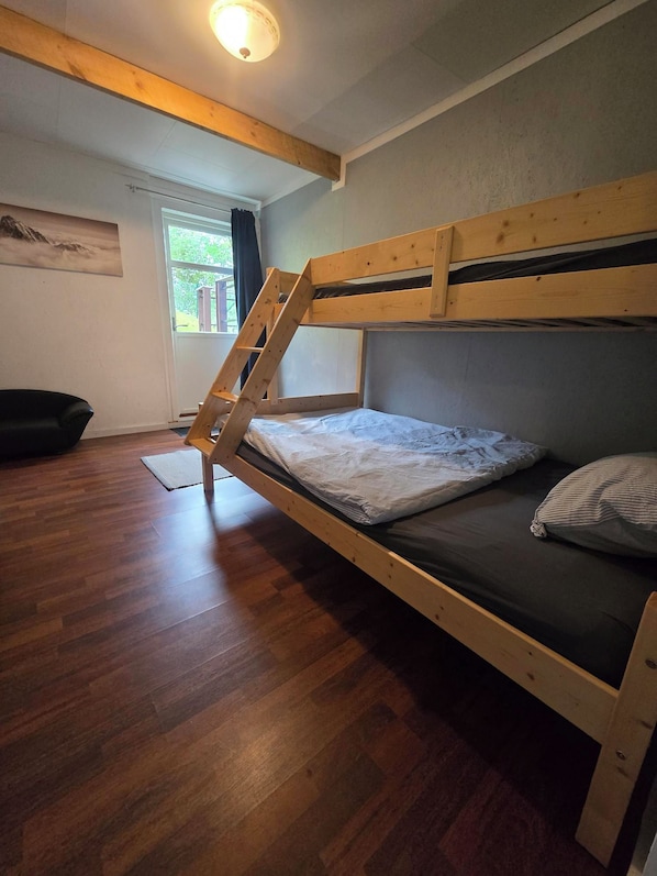 A bunk bed with a wooden ladder, a window with curtains, and a painting on the wall.