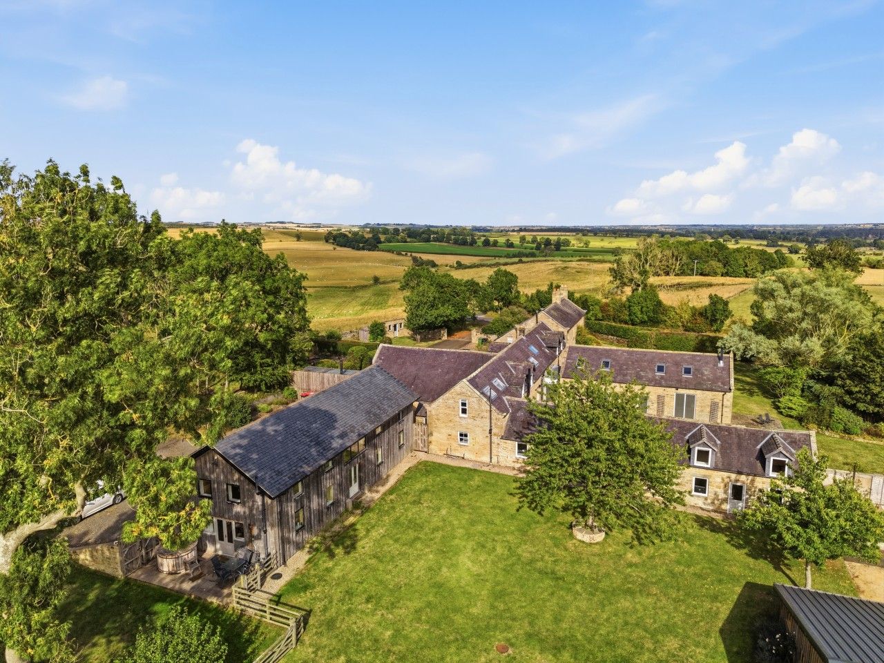 A large, rustic barn-style building with multiple rooms, surrounded by lush greenery and open fields.