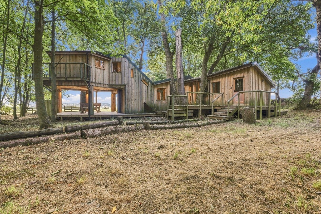 A rustic wooden cabin with a deck and a staircase leading to a second level.