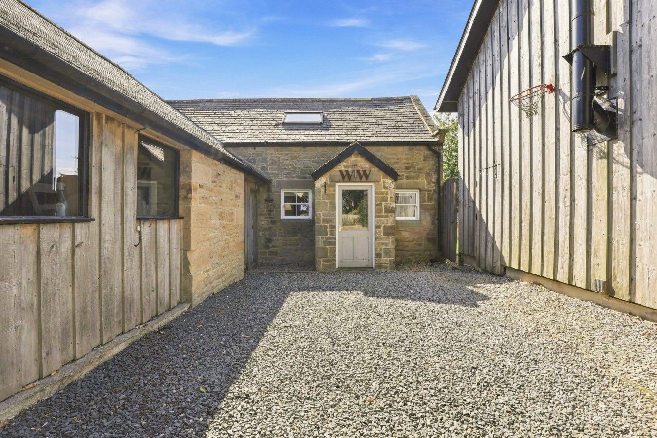 A stone building with a gravel driveway and wooden walls.