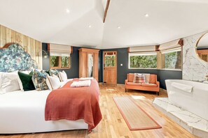 A bedroom with a large bed, a sofa, a window, and a bathroom with a bathtub. - Rose`s Bower Exclusive Hire - North East Escapes (Great Whittington)
