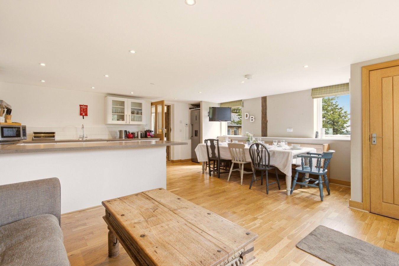 A modern kitchen with a dining area, wooden flooring, and a TV mounted on the wall.