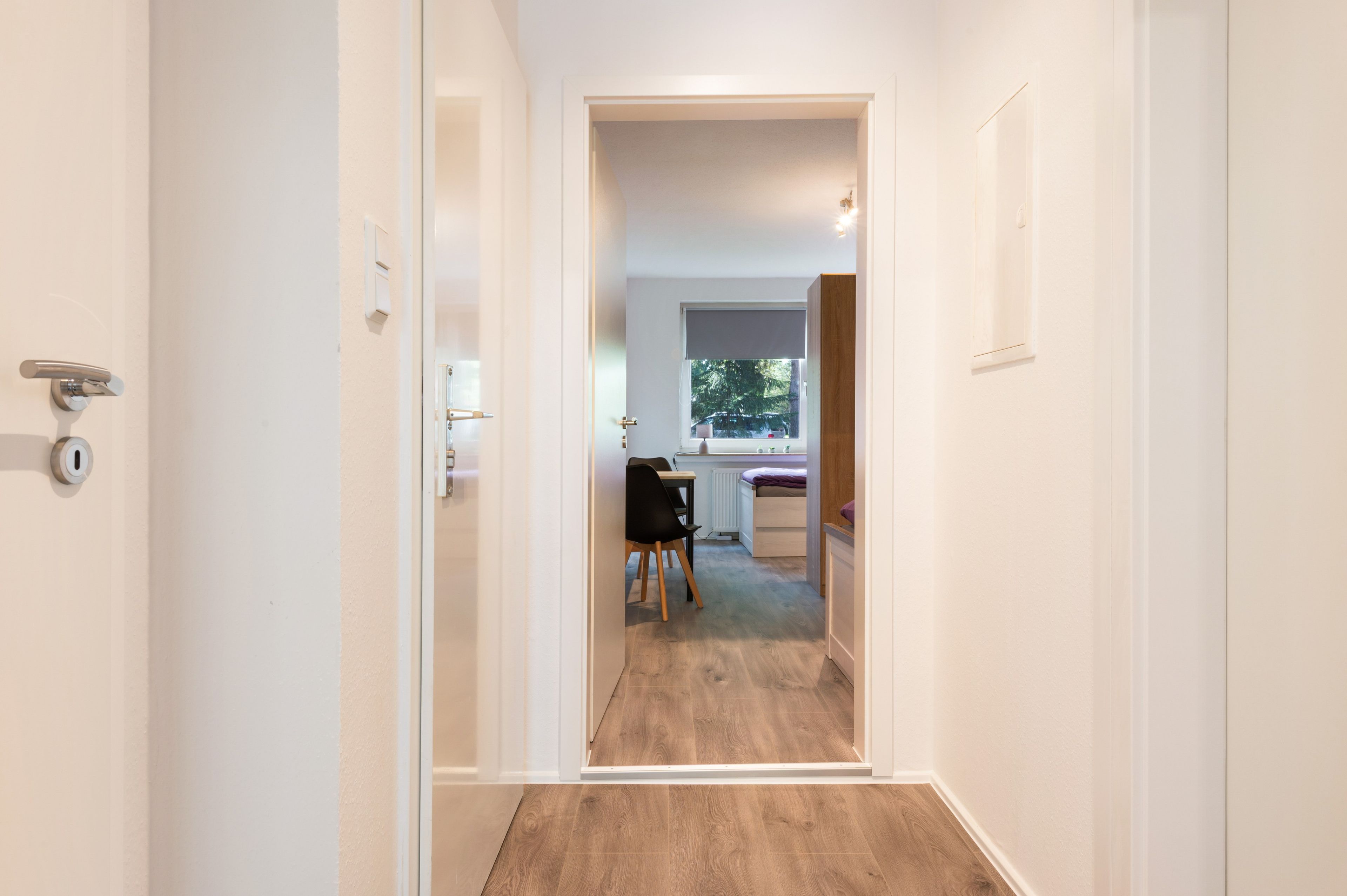 Un passadís que condueix a una habitació amb finestra, un radiador i una cadira.