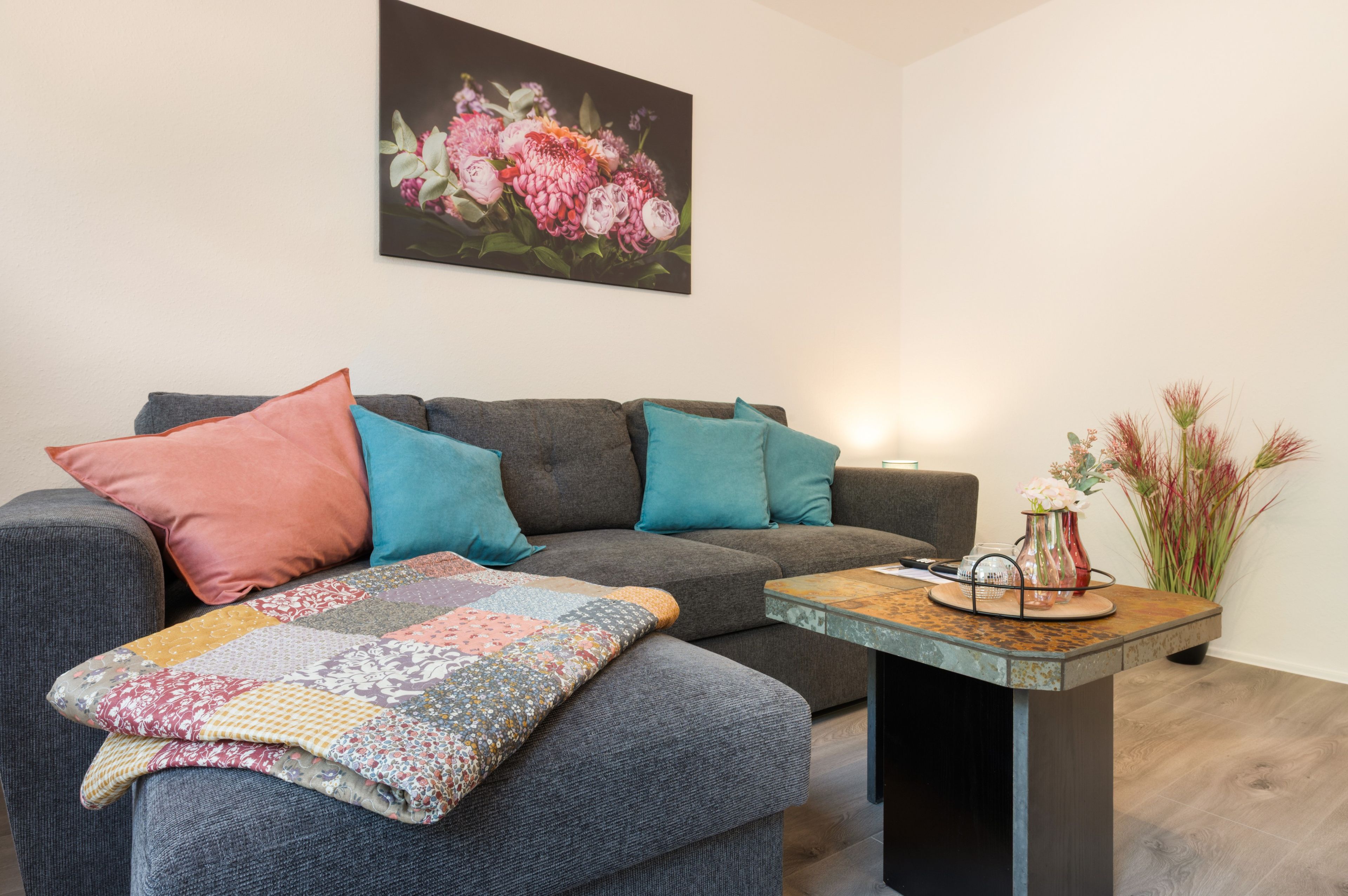 A living room with a grey sofa, colorful cushions, a patterned throw, and a small wooden coffee table with decorative items.