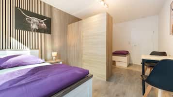 Ein modernes Schlafzimmer mit einem Bett, einem Schreibtisch und einem Stuhl. Es gibt einen Holzschrank und eine an der Wand befestigte Leuchte.