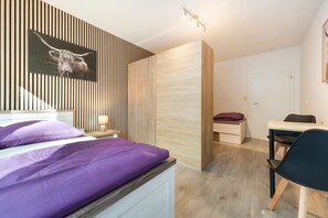 Ein modernes Schlafzimmer mit einem Bett, einem Schreibtisch und einem Stuhl. Es gibt einen Holzschrank und eine an der Wand befestigte Leuchte.