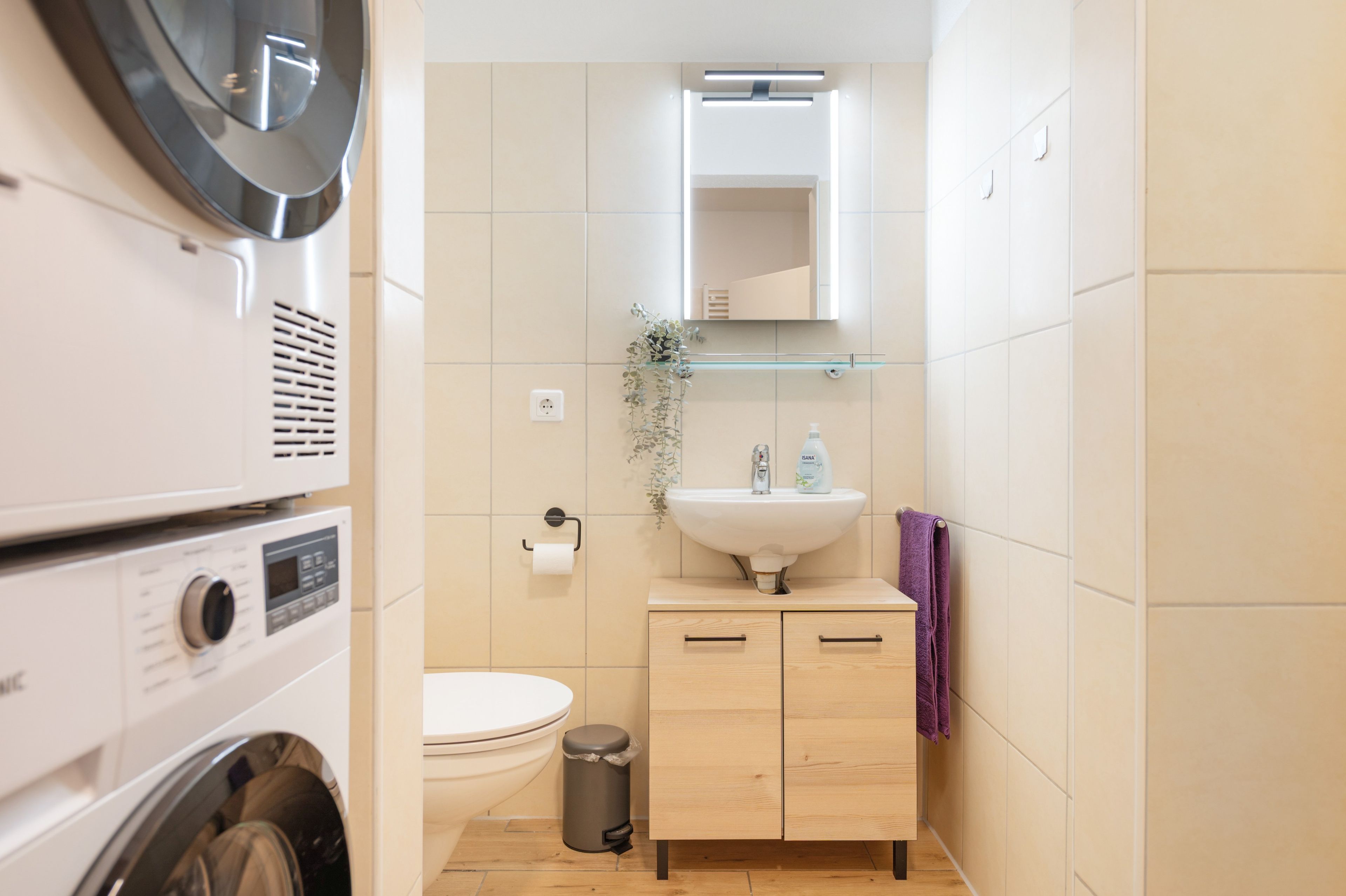 Ein kleines Badezimmer mit Waschmaschine, Toilette, Waschbecken und Spiegel.