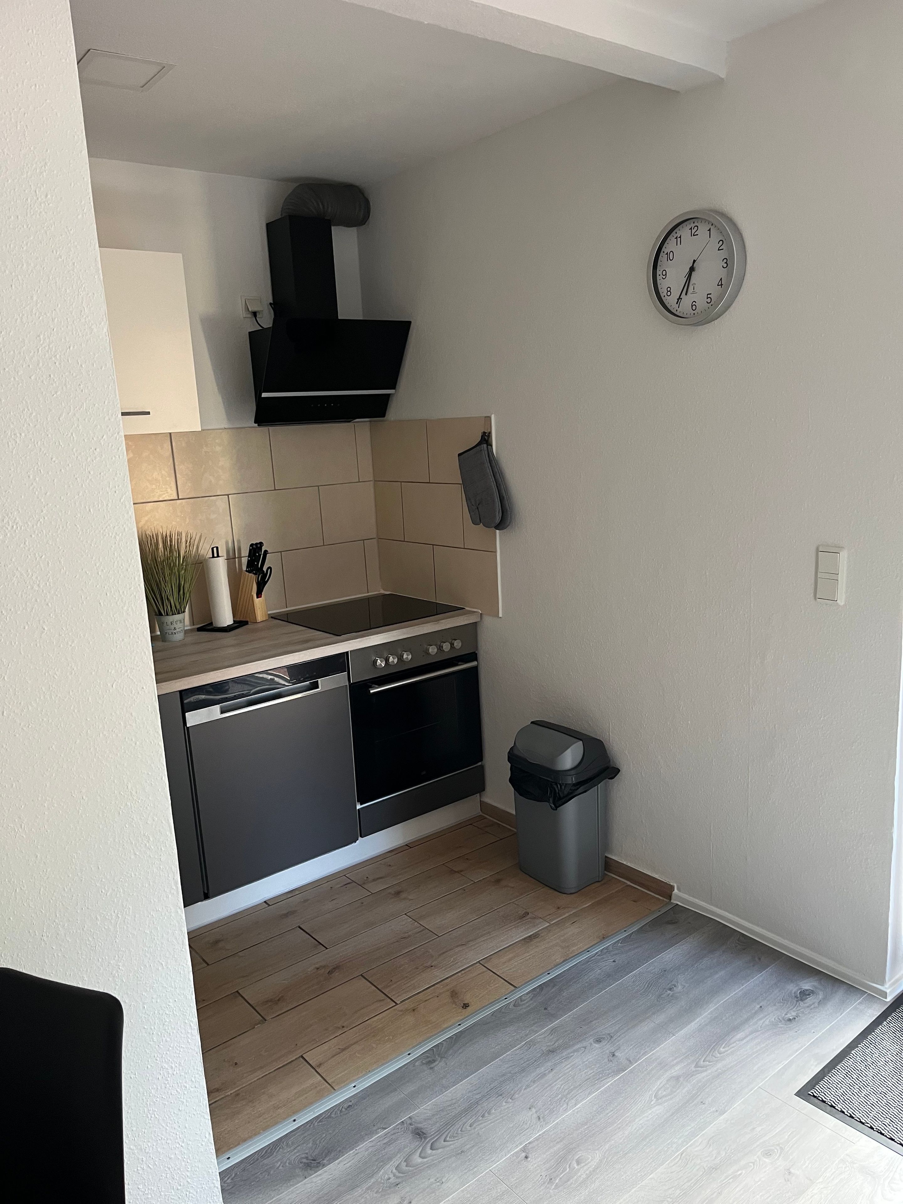A modern kitchen with a dishwasher, oven, and a clock on the wall.