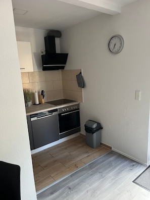 A modern kitchen with a dishwasher, oven, and a clock on the wall. - Apartment "Zum Waldblick 3" with Shared Garden and Wi-Fi (Wulsbüttel )