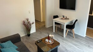 Uma sala de estar moderna com sofá, mesa de centro, mesa de jantar, cadeiras e TV de tela plana fixada na parede.