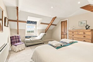 A bedroom with a sloped ceiling, a bed, a chair, a dresser, and a window with a view. - The Old Woodworker’s Cottage - North East Escapes (Great Whittington)